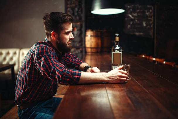 jonge man met fles whisky bij bar teller, alcoholisme, dronkenschap concept - Foto, afbeelding