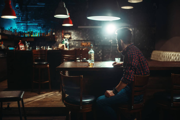 young man with bottle of whiskey at bar counter, alcoholism,  drunkenness concept - Фото, зображення