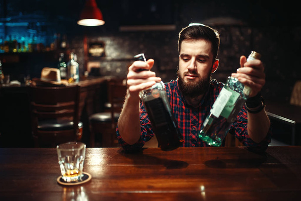 hombre sentado en el mostrador del bar con dos botellas de alcohol
 - Foto, Imagen