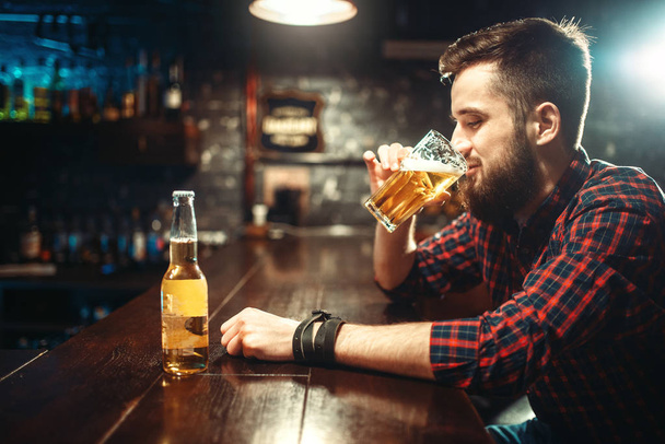 young bearded man drinking beer at bar counter in pub - Foto, Imagen
