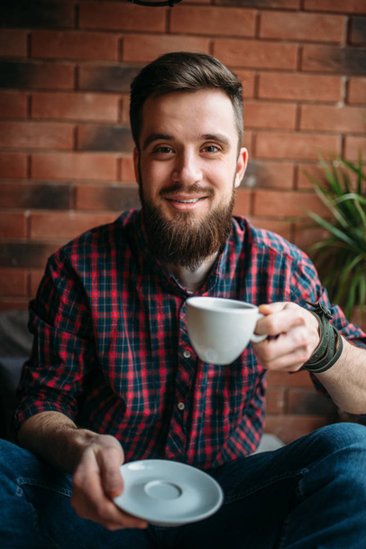 young man sitting in coffee house drinking beverage - 写真・画像