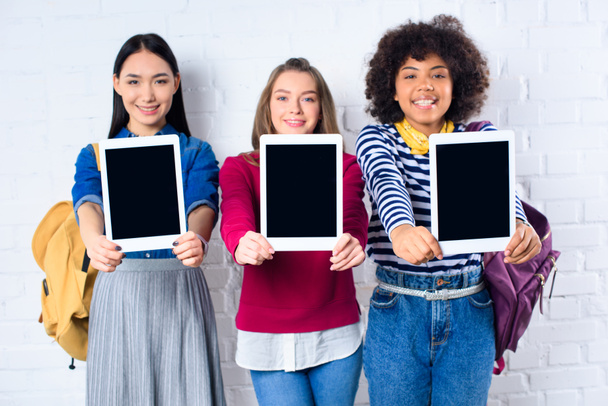 мультикультурные студенты, показывающие планшеты с чистыми экранами в руках у стены из белого кирпича
 - Фото, изображение