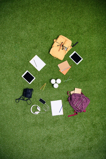 vista superior de los dispositivos digitales arreglados, mochilas y portátiles en el césped verde
 - Foto, Imagen