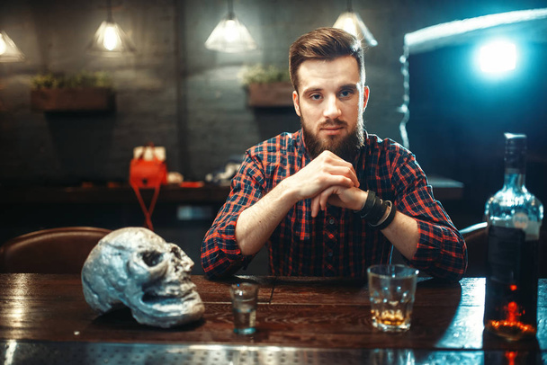 Trauriger Mann mit Totenkopf und Whiskeyflasche am Tresen, Alkoholsucht, Depressionen - Foto, Bild