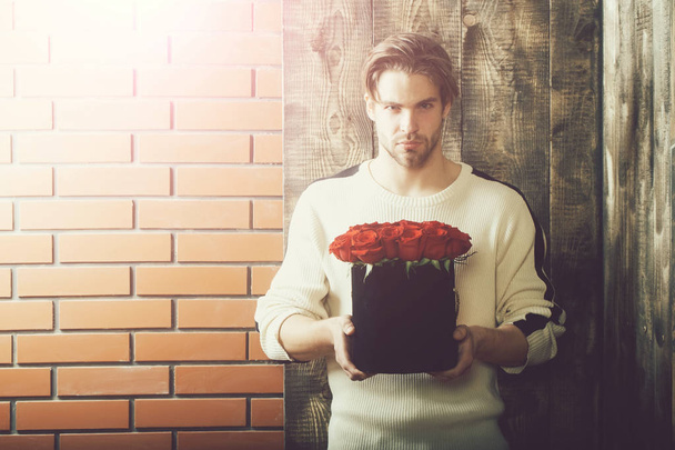 bearded man holds red rose flowers in box as present - Foto, afbeelding
