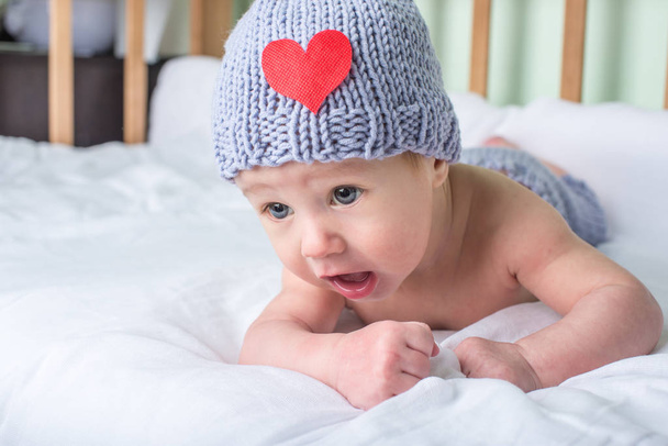 Счастливый малыш лежит в кроватке на одеяле в вязаной шапочке с сердцем. Концепция дикой природы материнства
 - Фото, изображение