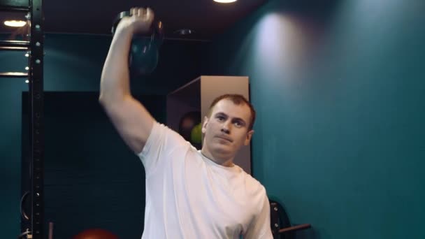 Fitness man doing a weight training by lifting heavy kettlebell. Yong athlete doing kettlebell swings. Bodybuilder lifting kettlebell - Πλάνα, βίντεο