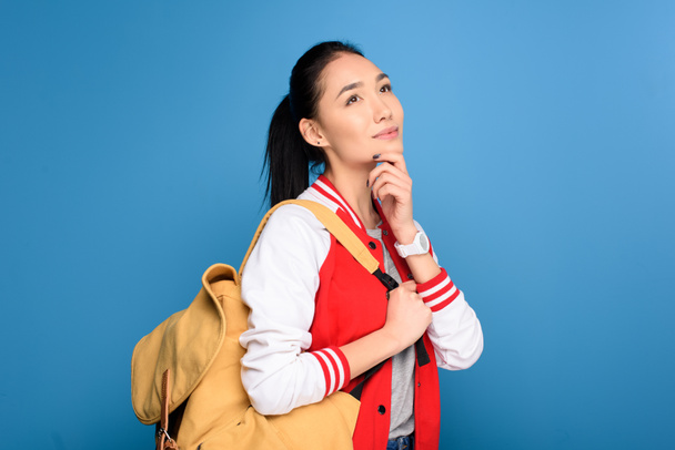 side view of pensive asian student with backpack isolated on blue - Φωτογραφία, εικόνα