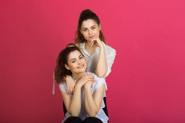 deux belles jeunes sœurs jumelles avec un sourire sur un fond rose
 - Photo, image