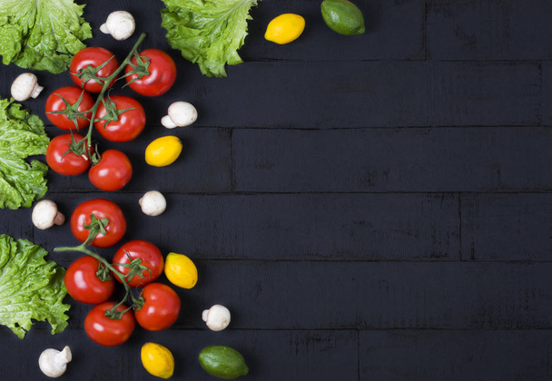 Red tomatoes with greens and lemons on a black wooden background. A composition of vegetables and fruits on a wooden background. - Фото, зображення