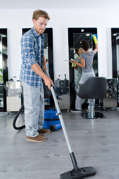 Mann reinigt Friseursalon mit Staubsauger - Foto, Bild