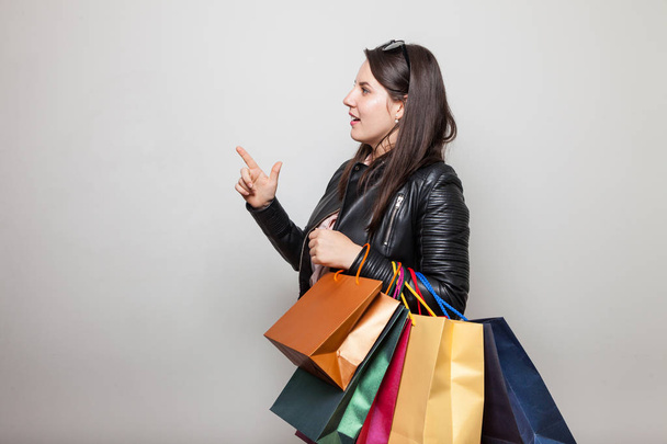 Linda chica joven con bolsas de compras apunta a una esquina de pie frente a un fondo blanco
 - Foto, imagen