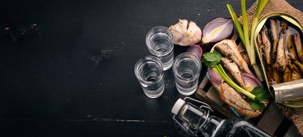 Vodka and a set of sandwiches with sprats, and caviar, onion and parsley, on a wooden background. Top view. Copy space. - Фото, изображение