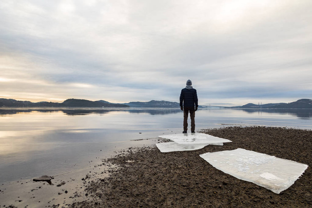 Mann steht am Strand, Eisschollen auf dunklem Sand, ruhige See, Nebel und Nebel. hamresanden, kristiansand, norwegen - Foto, Bild