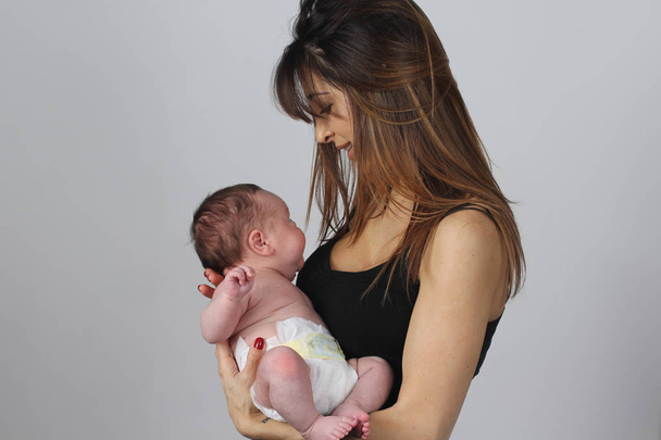 Nuori äiti pitelee pientä vauvaansa harmaalla taustalla
  - Valokuva, kuva