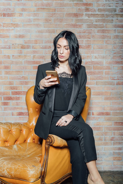 молодая красивая женщина позирует в помещении с помощью смартфона - блоггер, технологии, концепция моды
 - Фото, изображение