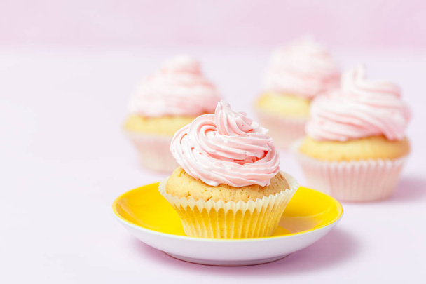 Cupcake decorated with pink buttercream in bright yellow plate on pastel pink background. Sweet beautiful cake. Horizontal banner, greeting card, congratulation. Close up photography. Selective focus - Fotó, kép