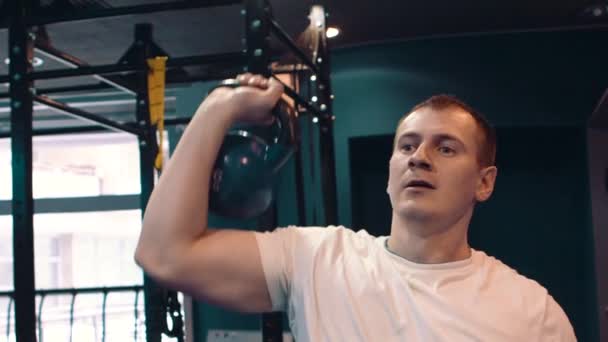 Fitness man doing a weight training by lifting heavy kettlebell. Yong athlete doing kettlebell swings. Bodybuilder lifting kettlebell - Filmagem, Vídeo