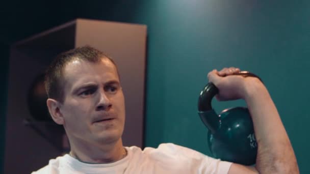 Fitness man doing a weight training by lifting heavy kettlebell. Yong athlete doing kettlebell swings. Bodybuilder lifting kettlebell - Záběry, video