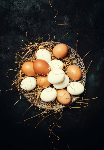 Multicolored chicken eggs with straw and branches, spring Easter composition, black background, top view - Zdjęcie, obraz