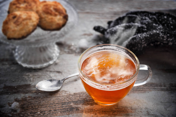 hot tea with steam in a glass cup on a wooden table, cookies and snowy gloves blurred in the background, best warm up after a winter walk - Fotografie, Obrázek