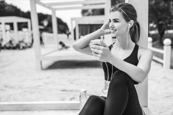 Pretty sporty girl with phone relaxing outdoor after training, black and white - Foto, Bild