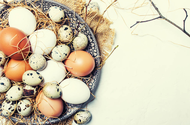Multicolored chicken and quail eggs with straw and branches, spring Easter composition, top view - Фото, зображення