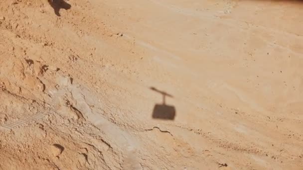 Shadow of a ropeway cabin rising in Masada desert. Aerial cable car going up on a sunny day. Sand and rocks. Israel 4K. - Filmati, video