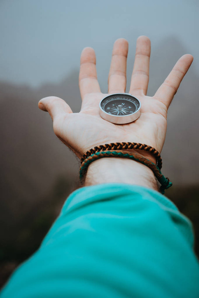 Stretched man arm with compass on the palm of the hand directed to mountain peaks on cloudy day - Foto, Imagem