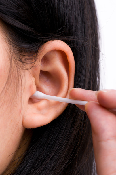Woman with black hairs is cleaning her ears with white cotton bud. Personal hygiene concept - Photo, Image