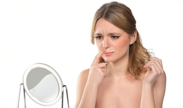 όμορφη νεαρή γυναίκα που αγγίζουν την μύτη της μπροστά από καθρέφτη. απομονωμένα σε λευκό φόντο - Φωτογραφία, εικόνα