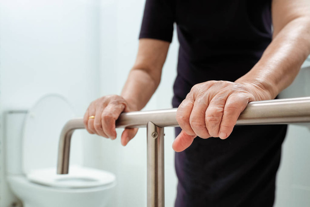 Elderly woman holding on handrail in bathroom. - Photo, Image