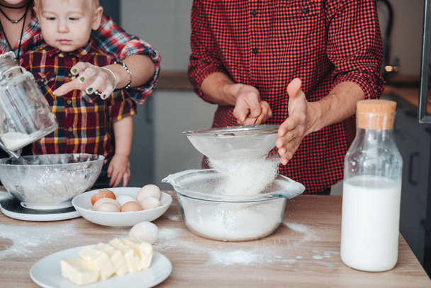 Isä seuloo jauhoja keittiössä
 - Valokuva, kuva