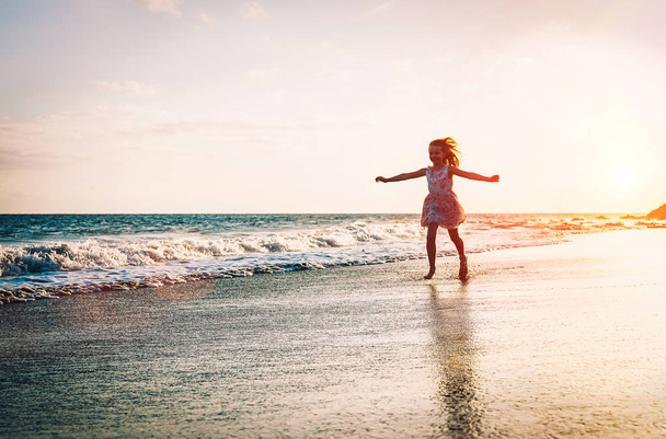 Happy little girl running inside water spreading her hands up on the beach - Baby having fun making splashing in the sea - Child, youth, happiness concept - Zdjęcie, obraz
