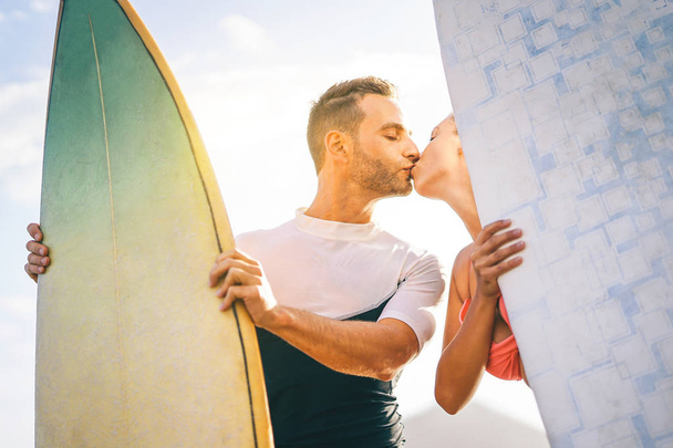 Młoda para zdrowia surferów Całowanie o zachodzie słońca na plaży trzymając deski surfingowe - miłośników szczęśliwy mając chwilę przetargu pocałunkiem podczas surfowania razem - ludzie, miłość, sport i lifestyle concept - Zdjęcie, obraz
