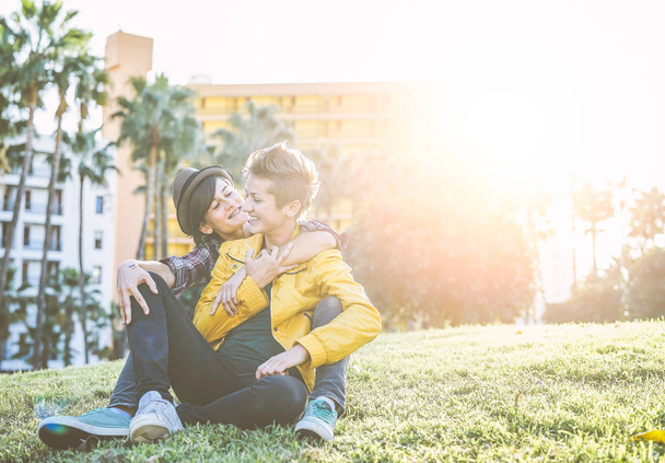 Feliz pareja gay abrazando y riendo juntos sentado en la hierba en un parque - Mujeres jóvenes lesbianas teniendo un momento tierno al aire libre - Lgbt, bisexualidad, relationship hsip concepto de estilo de vida
 - Foto, Imagen