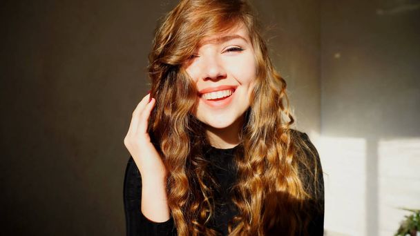 Mujer joven sonriendo, mirando a la cámara con el pelo rizado
 - Foto, Imagen