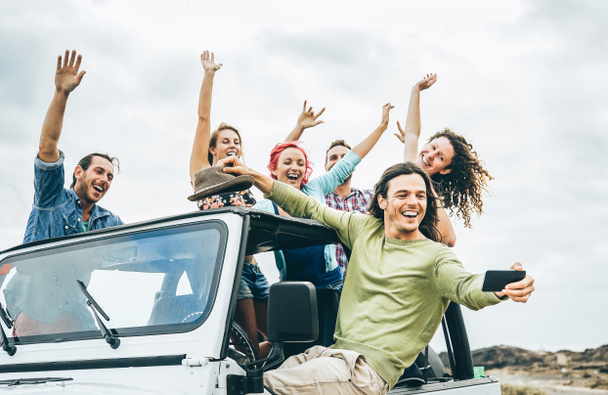 Grupo de amigos felices tomando selfie con el teléfono inteligente móvil en el coche jeep - Los jóvenes se divierten haciendo fotos durante su viaje por carretera - Amistad, vacaciones, vacaciones juveniles concepto de estilo de vida
 - Foto, Imagen
