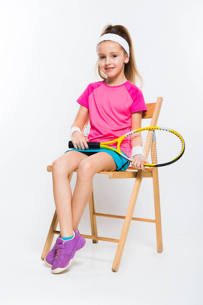 Tahta sandalyede oturan ve kameraya gülümseyen sevimli küçük tenis oyuncusu  - Fotoğraf, Görsel