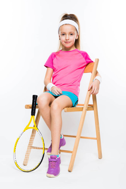Niedliche kleine Tennisspielerin sitzt auf einem Holzstuhl und lächelt in die Kamera  - Foto, Bild