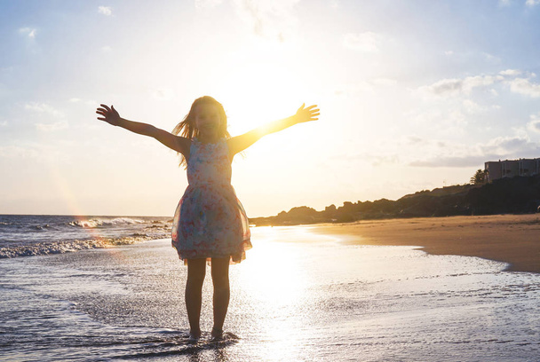 Happy child spreading her hands up on the beach on a magnificent sunset - Baby girl having fun in vacation holidays - Childhood, children, happiness concept - Foto, imagen