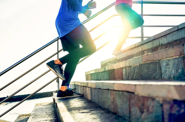 Couple running on stairs at sunset - Friends making a workout session exercising to get on staircase outdoor - Close up legs of people running - Sport, Health, lifestyle people concept - Photo, Image