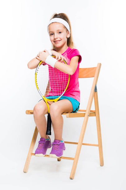 niedliches kleines Mädchen sitzt auf Stuhl und hält Squash-Schläger  - Foto, Bild