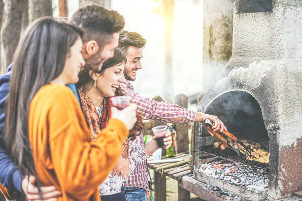 Young people having a barbecue party in the backyard on mountain - Happy friends grilling meat and drinking red wine outdoor - Friendship, lifestyle and food concept - Focus on male hand right - Photo, Image
