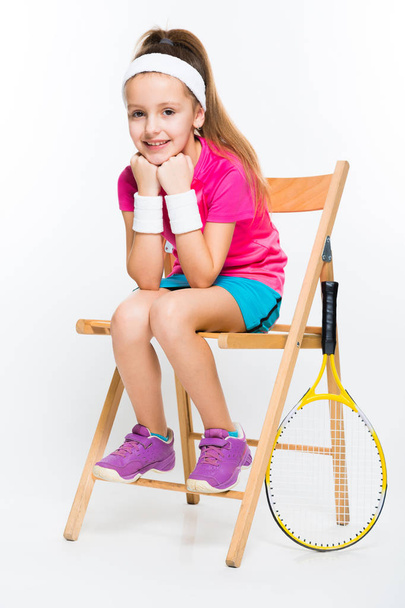 Cute little tennis player sitting on wooden chair and looking at camera  - Photo, Image
