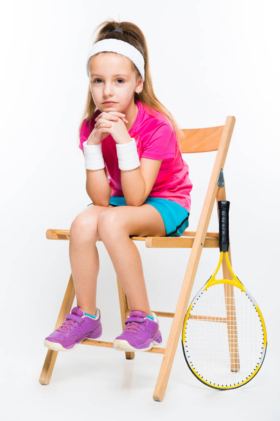 Niedliche kleine Tennisspielerin sitzt auf einem Holzstuhl und blickt in die Kamera  - Foto, Bild