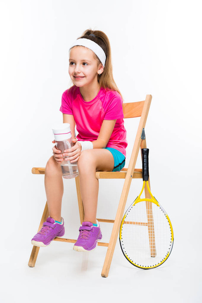 Cute little tennis player sitting on wooden chair and holding bottle of water  - Foto, immagini