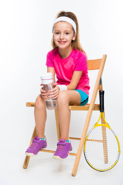 Cute little tennis player sitting on wooden chair and holding bottle of water  - Photo, Image
