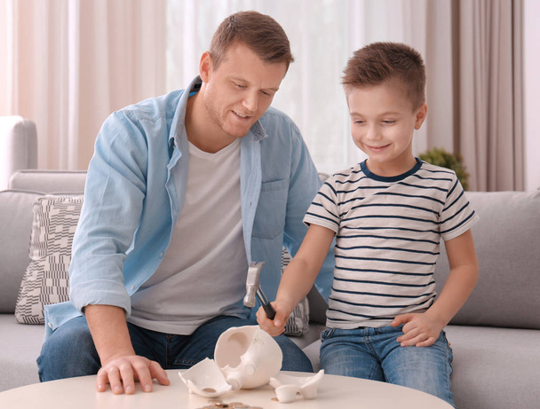 Father with little son breaking piggy bank with hammer at home - Foto, immagini