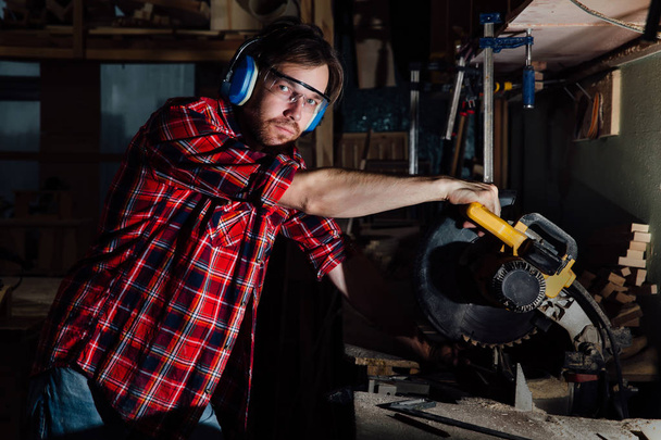 brunette man profession carpenter builder saws with a circular saw a wooden board. - 写真・画像
